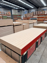Stack of grooved plywood sheets in a warehouse with shelving and pallet storage