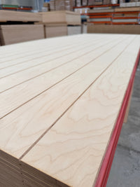 Stack of grooved plywood panels with light wood grain in a warehouse setting
