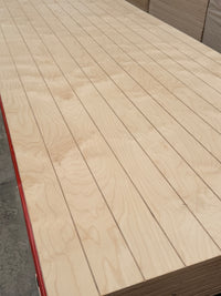Stack of grooved plywood sheets with a light wood grain finish in a warehouse setting