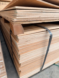 Stack of plywood sheets on a pallet in a warehouse, secured with black straps