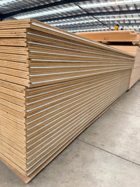 Stack of plywood sheets in a warehouse, showing layered wood grain and smooth edges.