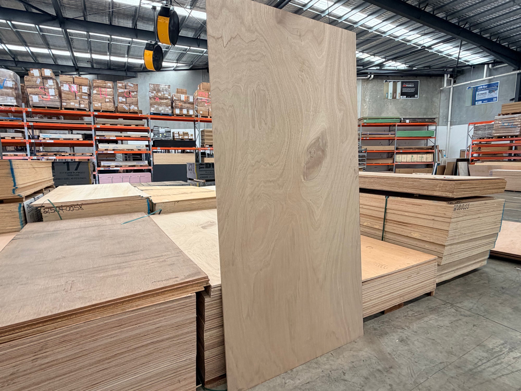 Large marine plywood sheet standing vertically in a warehouse with stacked plywood sheets