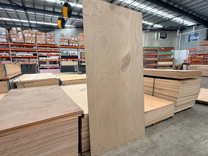 Large marine plywood sheet standing vertically in a warehouse with stacked plywood sheets