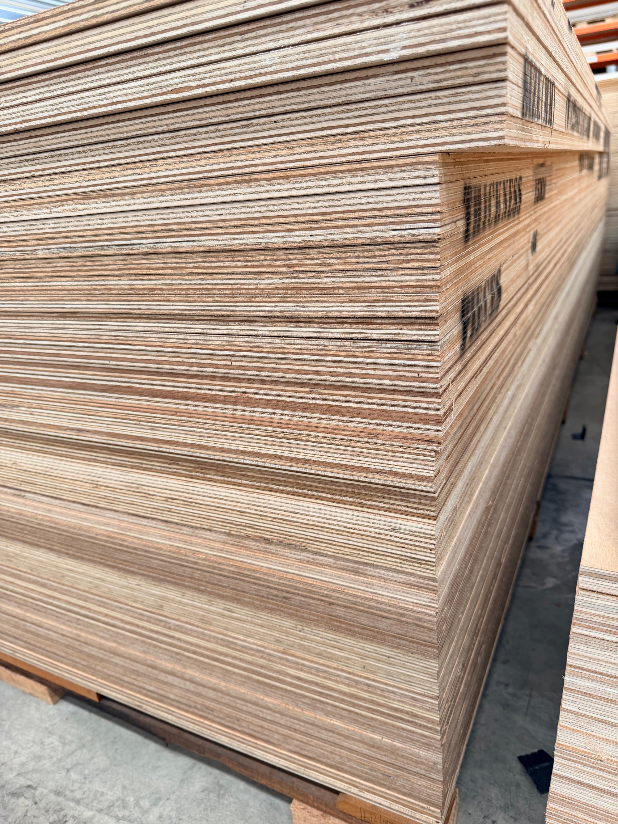 Stack of marine plywood sheets on a pallet in a warehouse, plywood grain visible