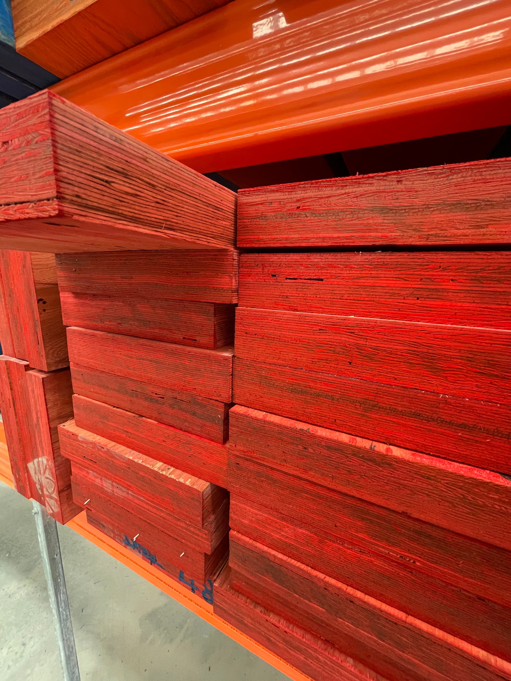 Stack of red H2S treated LVL beams on warehouse racking, end view showing laminated veneers - Just Plywood Melbourne